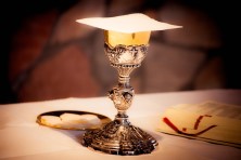 A chalice with wine on a table next to an open bible