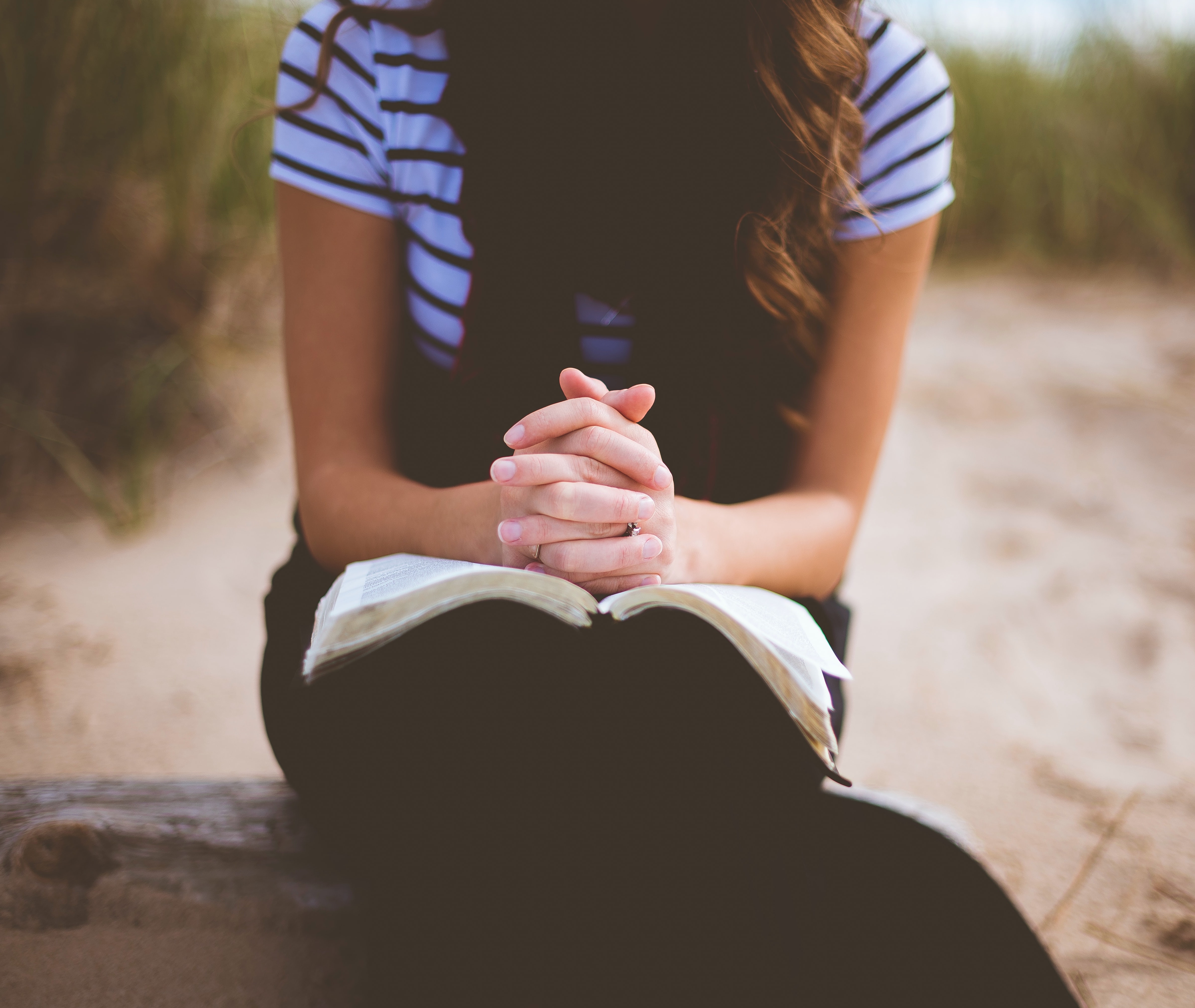 woman sitting on a log with bible on her lap praying and reflecting