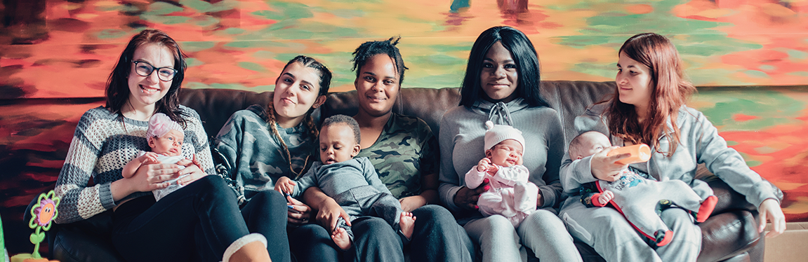 5 women's sitting on a couch with 4 little baby's.